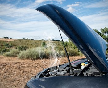 Close up of a broken down car, engine open with smoke, in a rural area