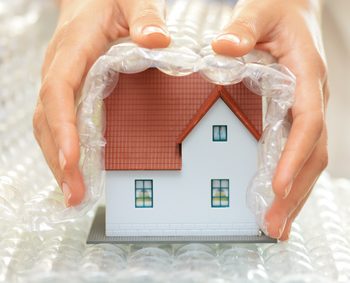 Woman hands covering a model house with bubble wrap- house protection or insurance concept